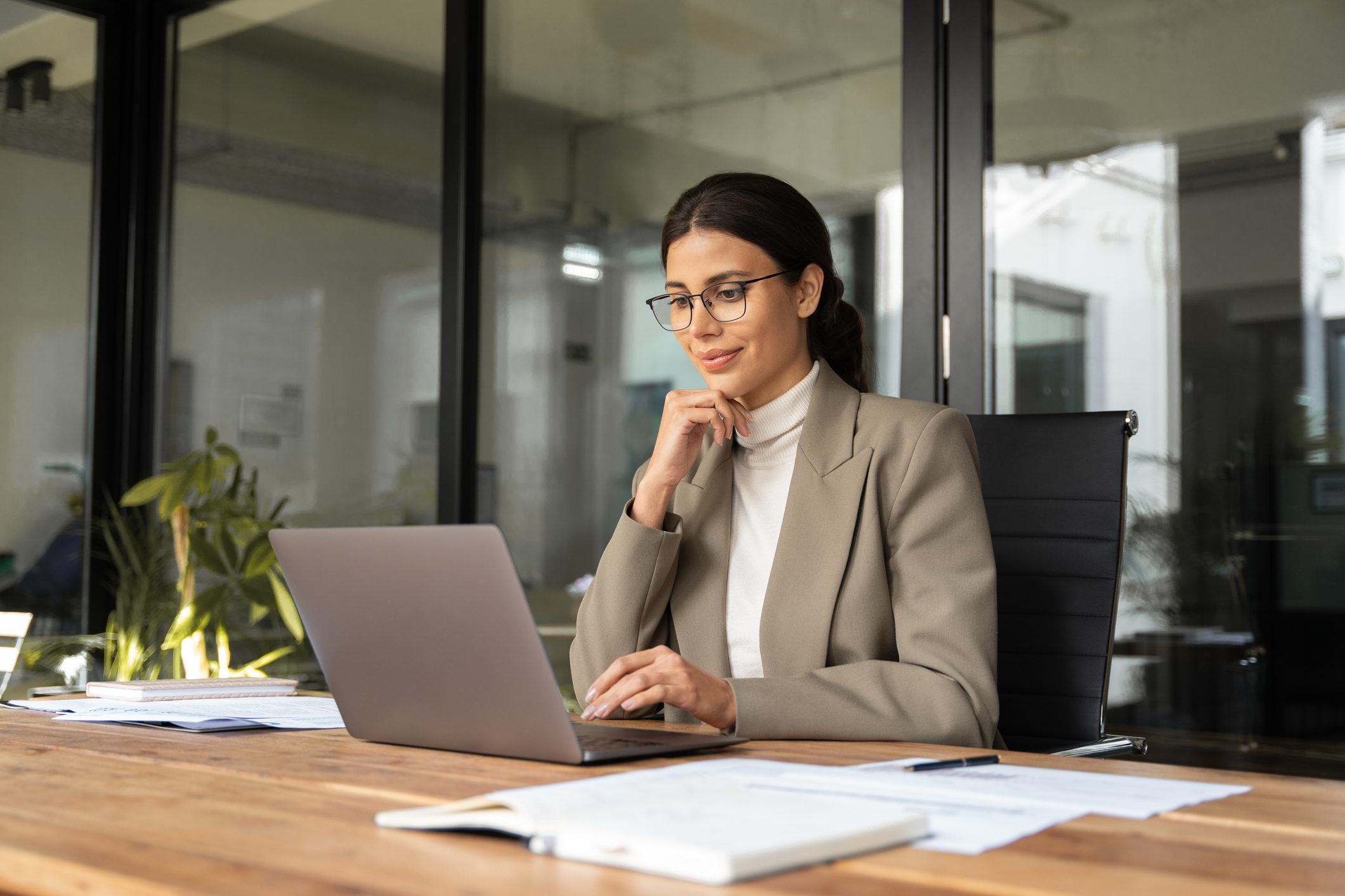 Professional woman working thoughtfully on a laptop in a modern office.